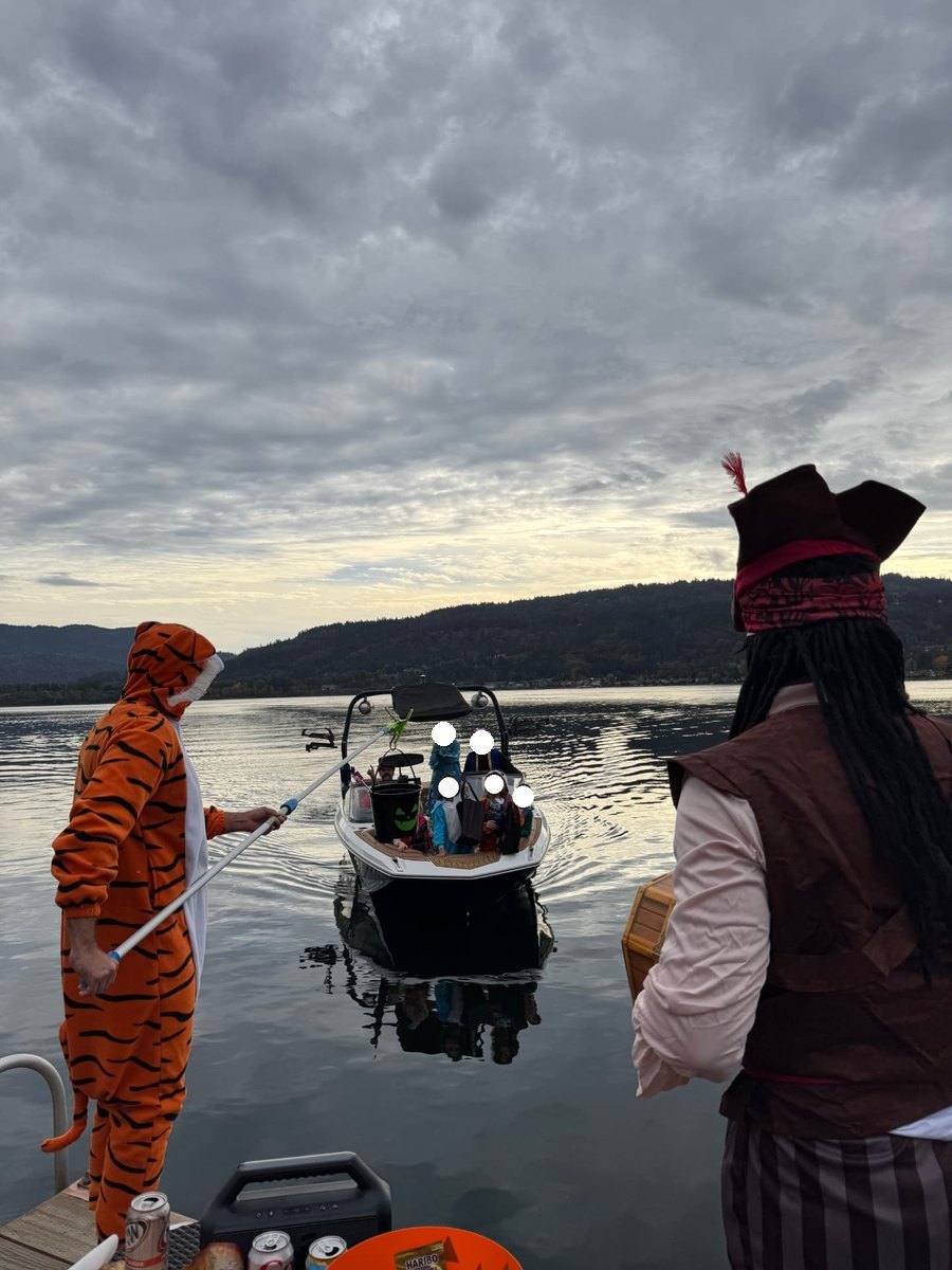 A boat of trick-or-treaters pulling up to a dock while treats are handed over on a pole