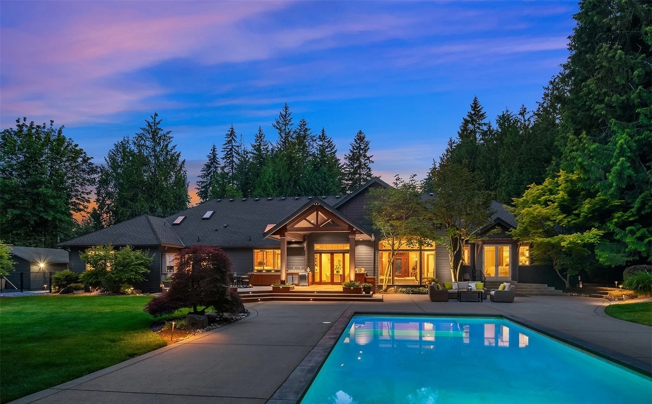 Northwest estate at dusk with a lit pool and wide lawn framed by evergreens